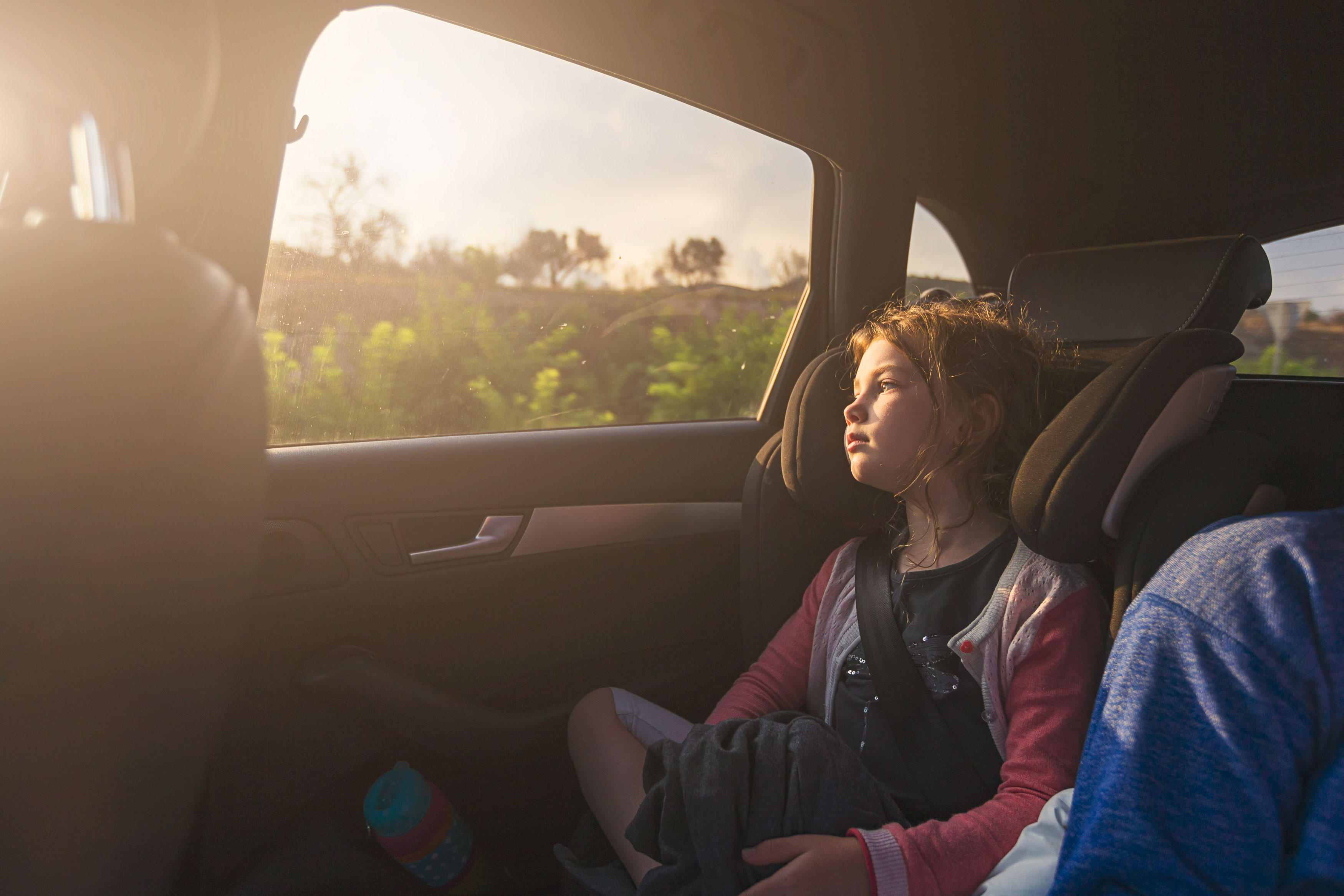 A child is sitting in the back of a car and is looking dreamily through the car window