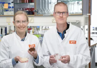 Two researchers smiling at the camera wearing VTT lab coats