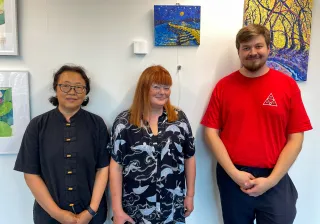 Three art club members standing in front of their art and smiling at the camera.