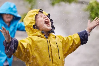 Two children are playing in the rain while the child in front is catching rain drops in their mouth