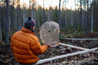 A man is lifting á round piece of ice and looking through it in a forest