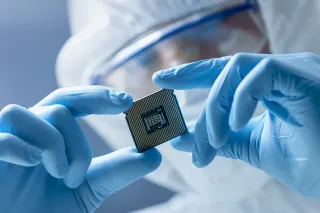 A photo of a person wearing rubber gloves, a face guard and protective overalls examining a microchip.