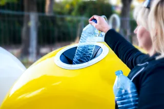 A photo of a person putting plastic bottles into a recycling bin.