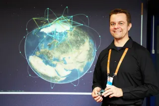 A smiling man , Dr Marko Höyhtyä, standing in front of a space illustration