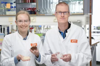 Two researchers smiling at the camera wearing VTT lab coats